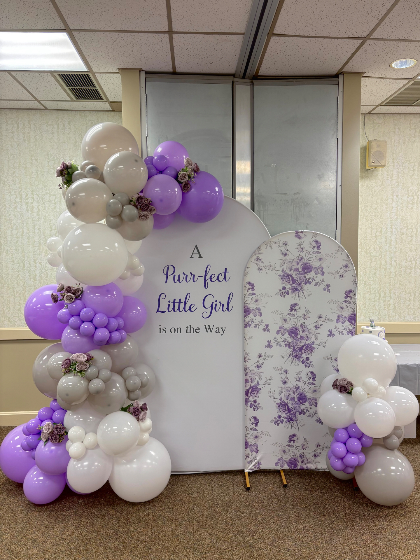 Purple, lavender, white and grey balloon garland on a double arch with floral panel for a baby shower