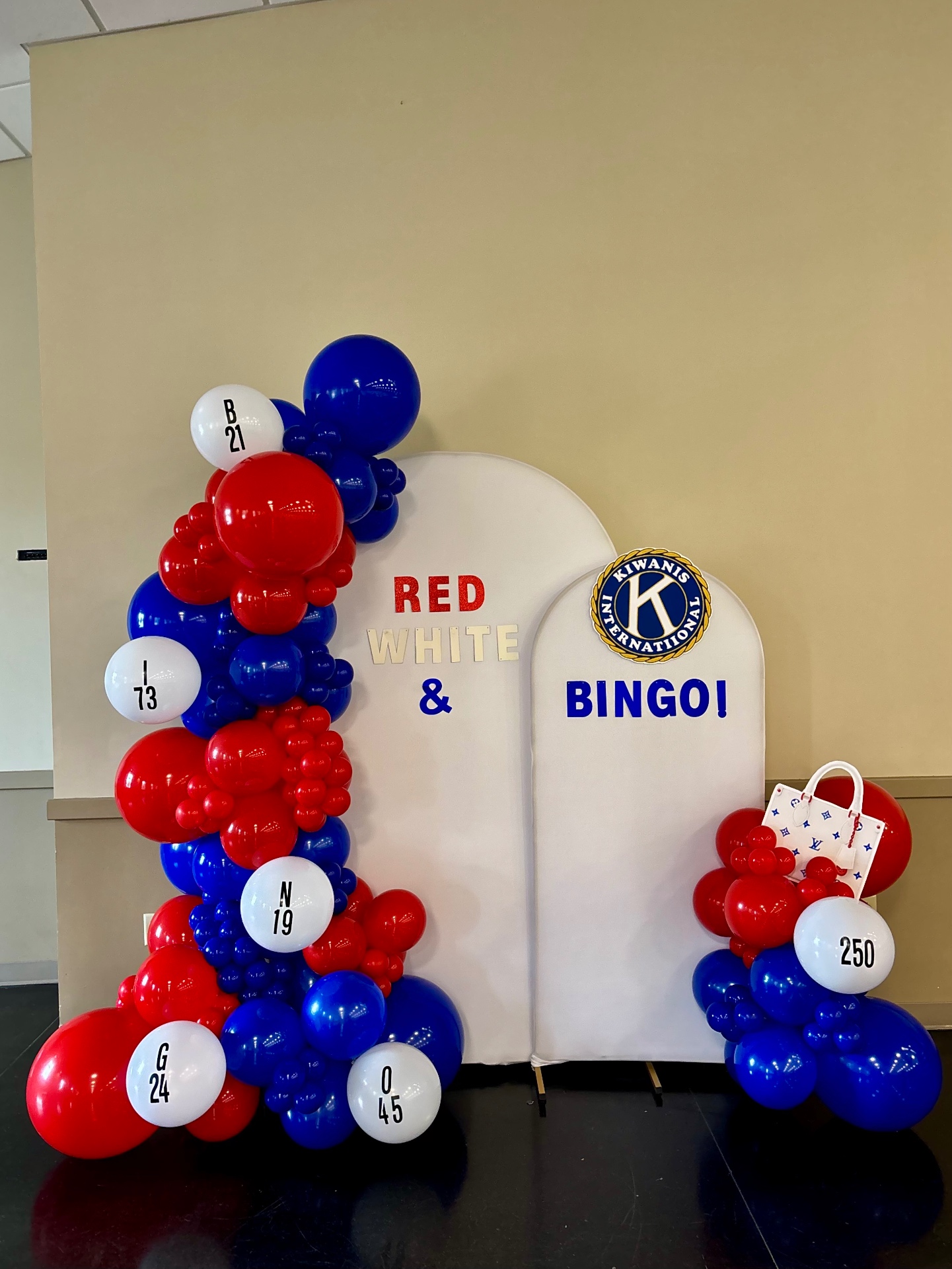 Red, white and blue balloon garland with bingo ball accents beside a Kiwanis Red White & Bingo arch